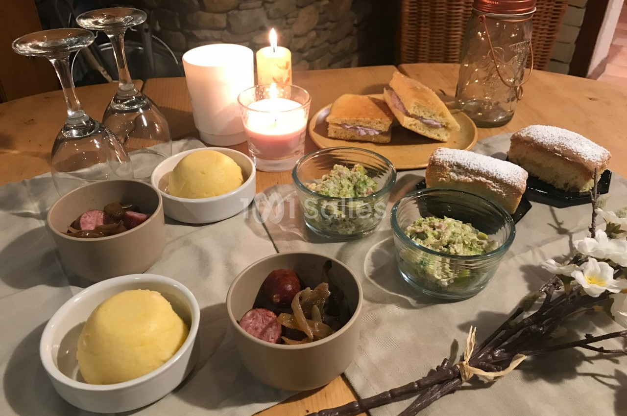 Repas convivial avec polenta, saucisses, salade composée, pâtisseries et bougies sur une table en bois.