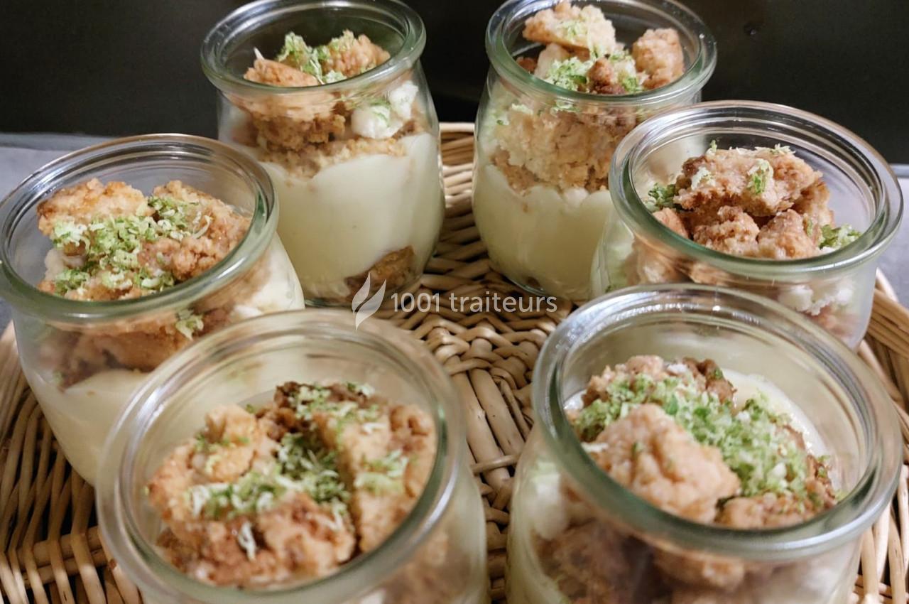 Desserts en verrines avec une base crémeuse, crumble doré et zestes verts, présentés sur un plateau en osier.