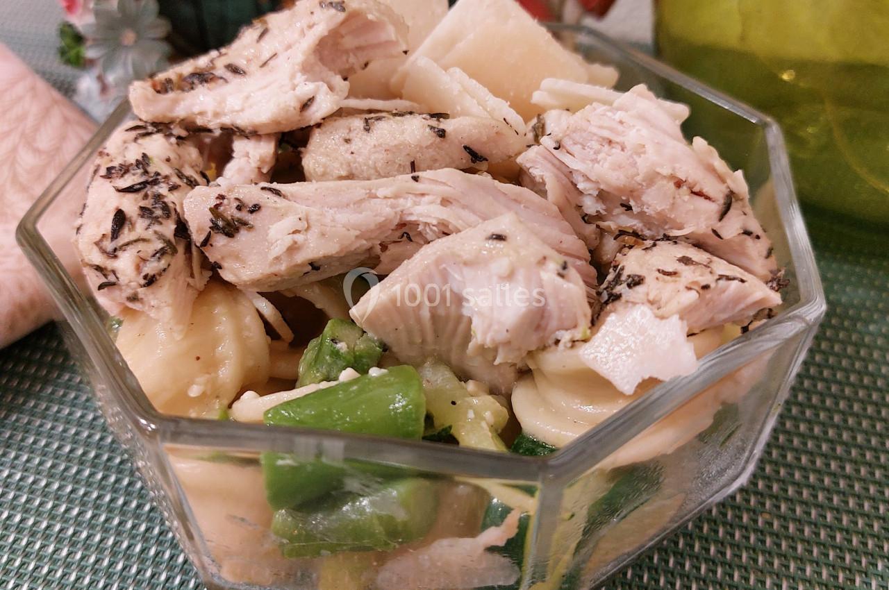 Salade composée avec pâtes, morceaux de poulet assaisonné et légumes verts, servie dans un bol en verre.