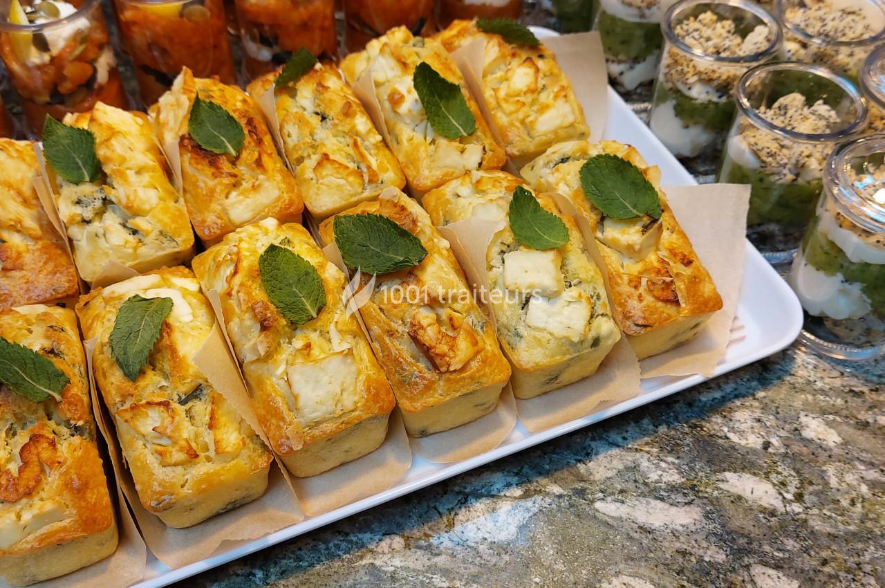 Plateau de mini cakes salés garnis de fromage et décorés de feuilles de menthe, accompagnés de verrines sucrées.