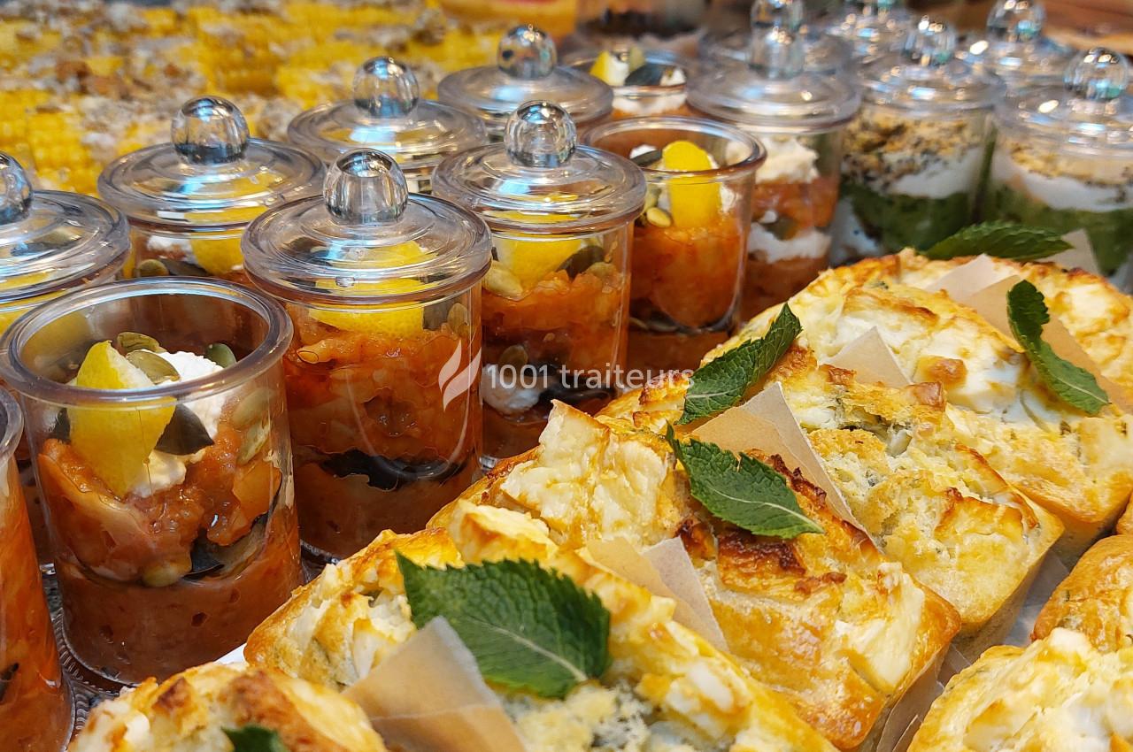 Buffet avec verrines colorées, tartes salées garnies de menthe et desserts variés présentés sur une table.