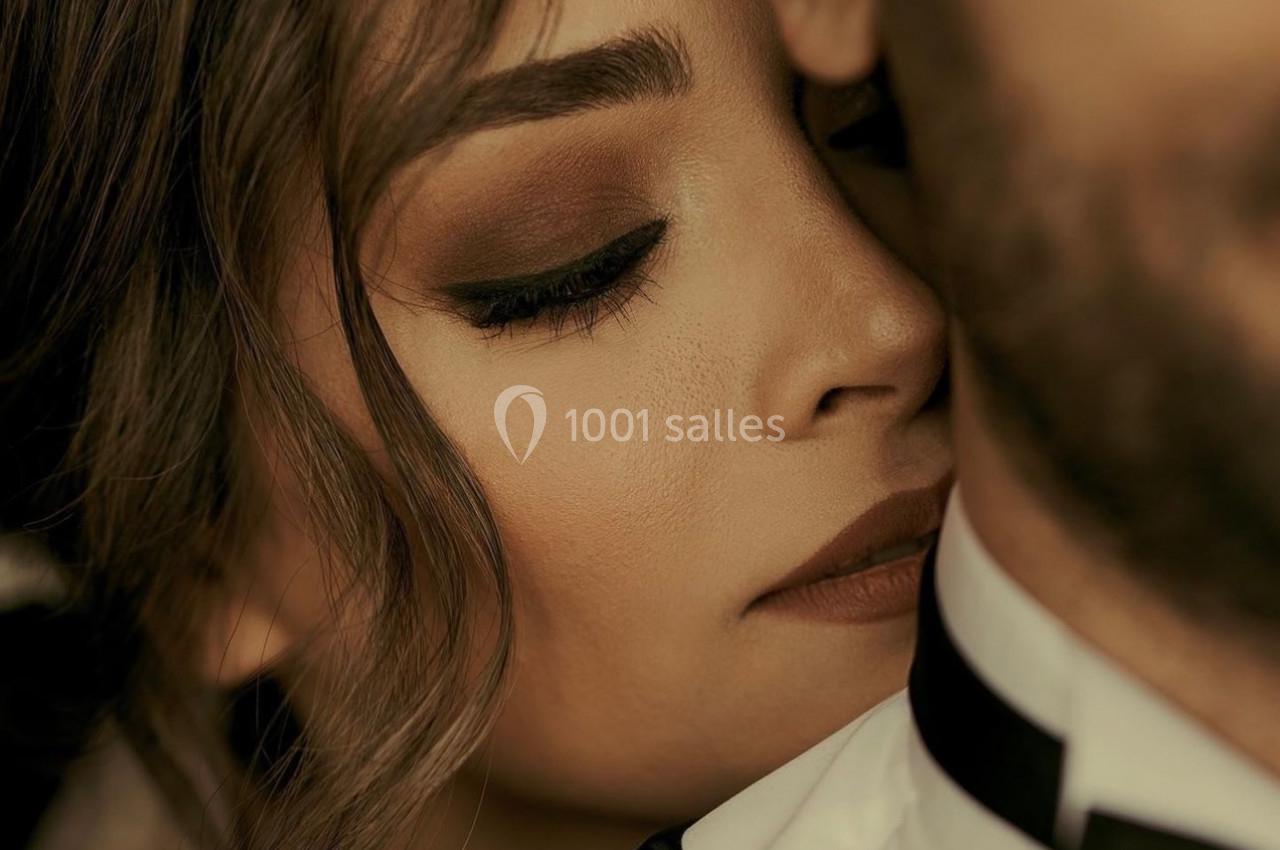 Femme au maquillage soigné posant son visage contre l'épaule d'un homme en costume, dans une ambiance intime.