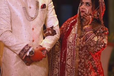 Un couple en tenue de mariage traditionnelle, l'homme en sherwani blanc et la femme en robe brodée rouge.