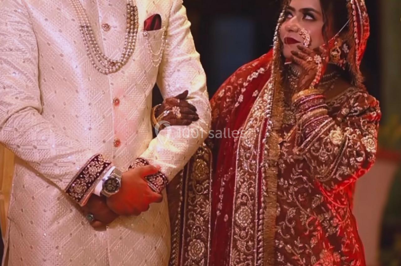 Un couple en tenue traditionnelle de mariage, l'homme en sherwani clair et la femme en sari rouge orné de broderies.