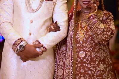 Un couple en tenue de mariage traditionnelle, l'homme en sherwani blanc et la femme en robe brodée rouge.