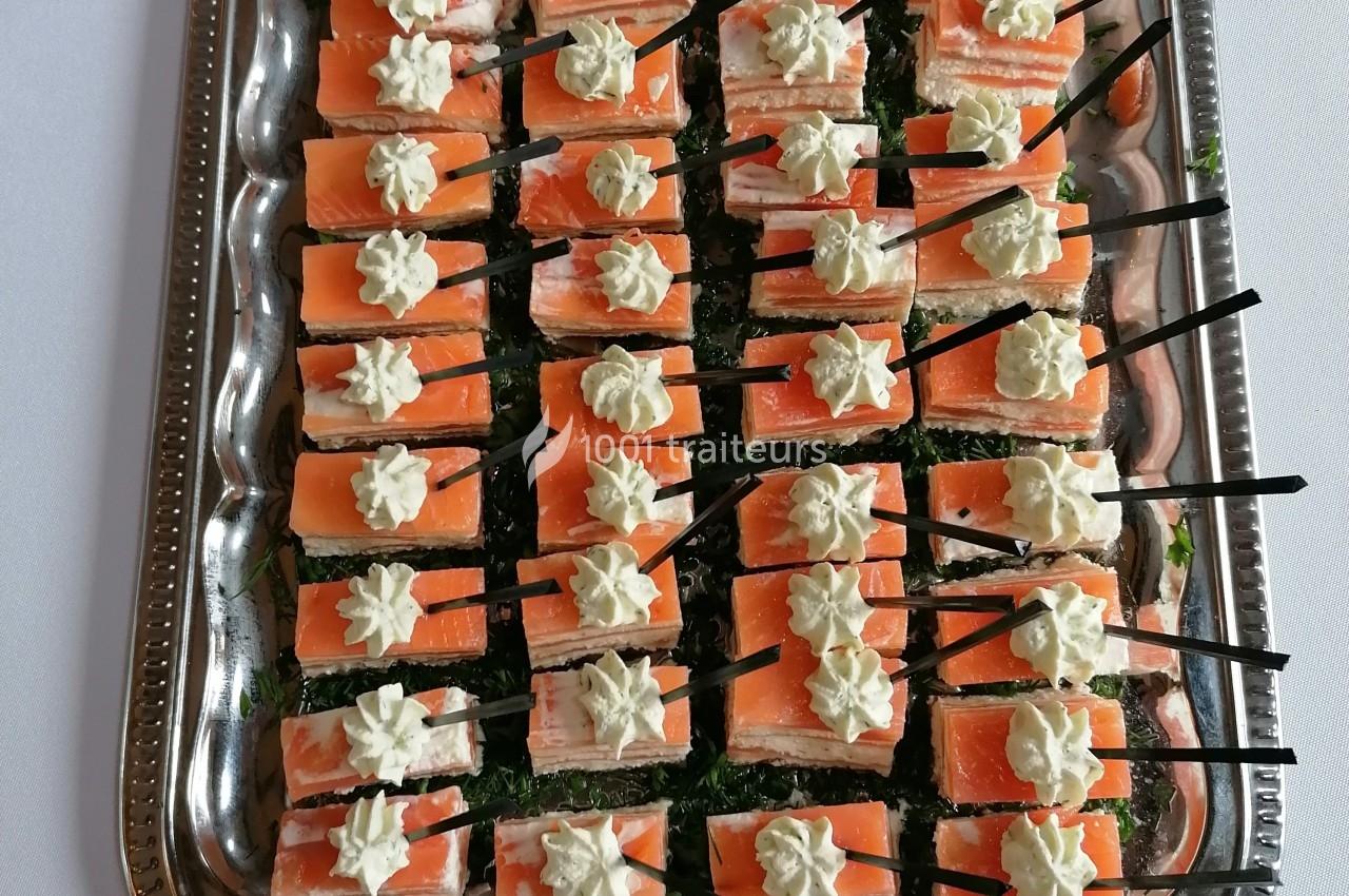 Plateau de bouchées apéritives au saumon fumé, garnies de crème et présentées avec des piques noires.