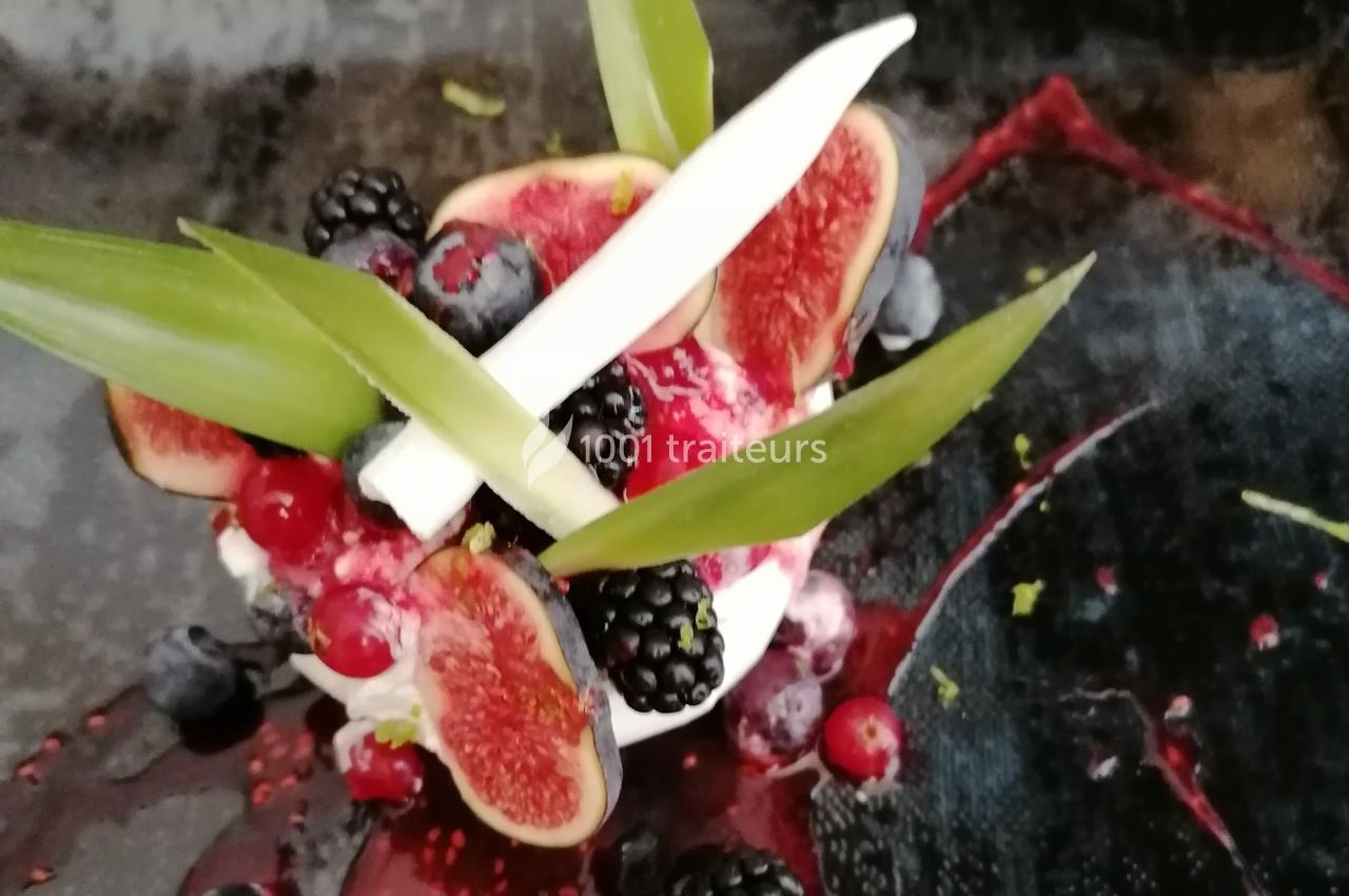 Dessert décoré de figues, mûres, groseilles, myrtilles, feuilles vertes et éclats blancs sur une assiette sombre.