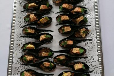 Cuillères apéritives noires garnies de morceaux de foie gras, herbes fraîches et accompagnements, présentées sur un plateau…