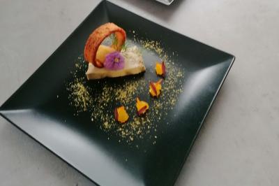 Dessert élégant sur assiette noire, décoré de fleurs comestibles, d'un biscuit courbé et de poudre colorée.