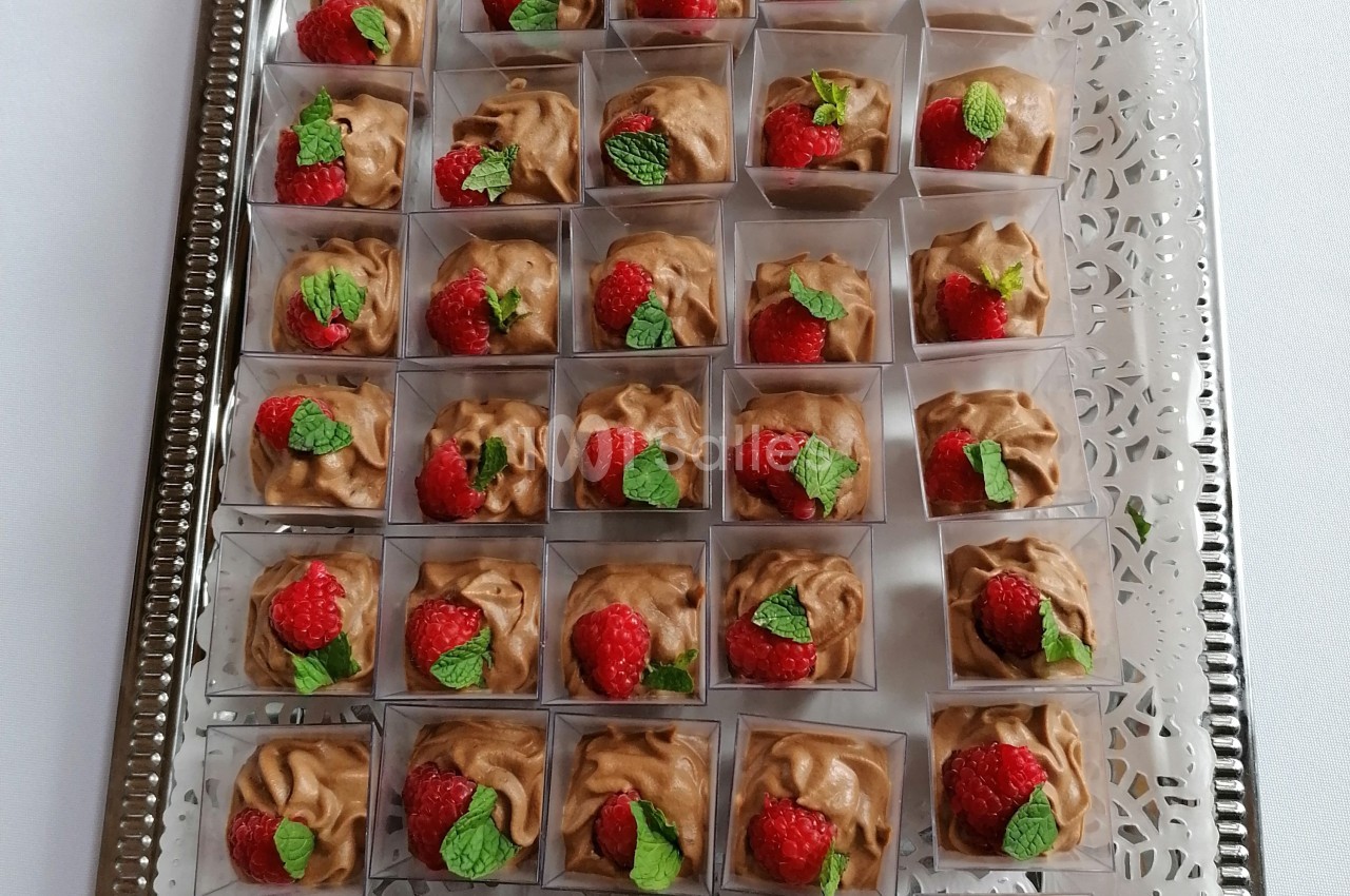 Dessert en portions individuelles avec mousse au chocolat, framboises et feuilles de menthe, disposé sur un plateau argenté.