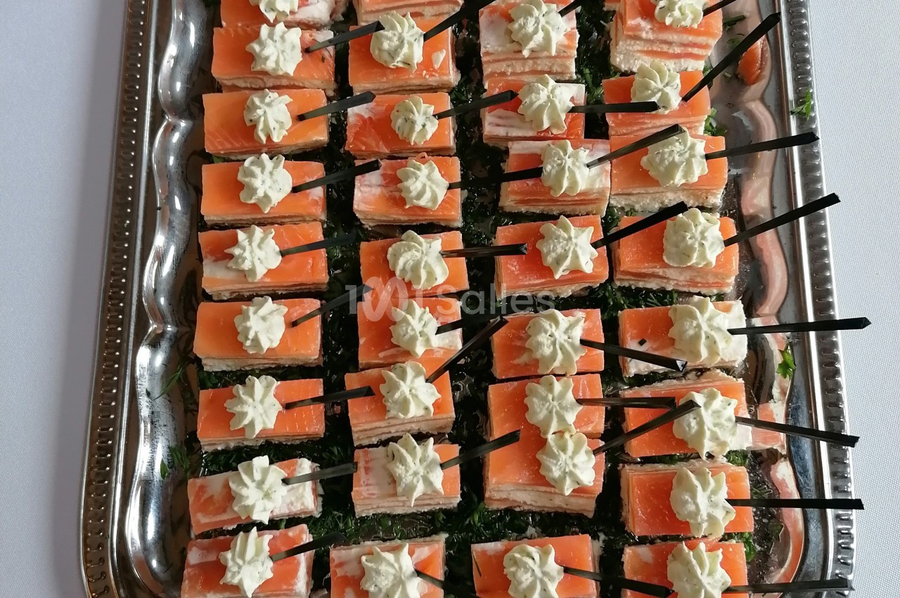 Plateau de bouchées apéritives au saumon fumé, garnies de crème et présentées avec des piques noires.