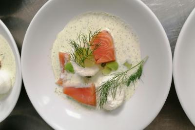 Assiette contenant du saumon fumé, crème, herbes fraîches et garnitures sur une sauce blanche.