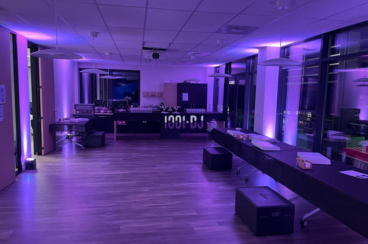 Salle moderne avec éclairage violet, tables alignées, équipement audio et grandes baies vitrées donnant sur l'extérieur.