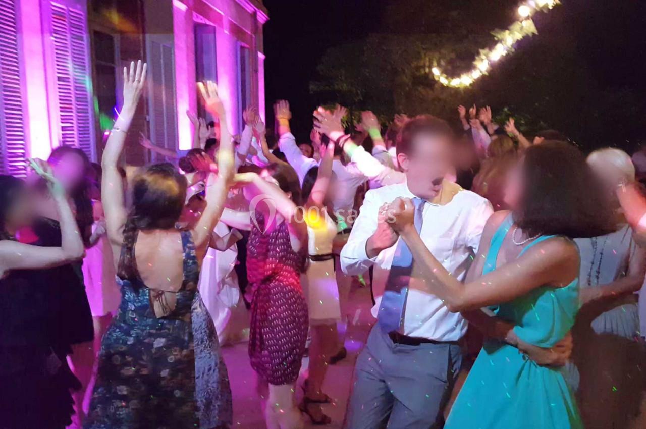 Personnes dansant lors d'une fête en soirée, éclairées par des lumières colorées et entourées d'une ambiance festive.