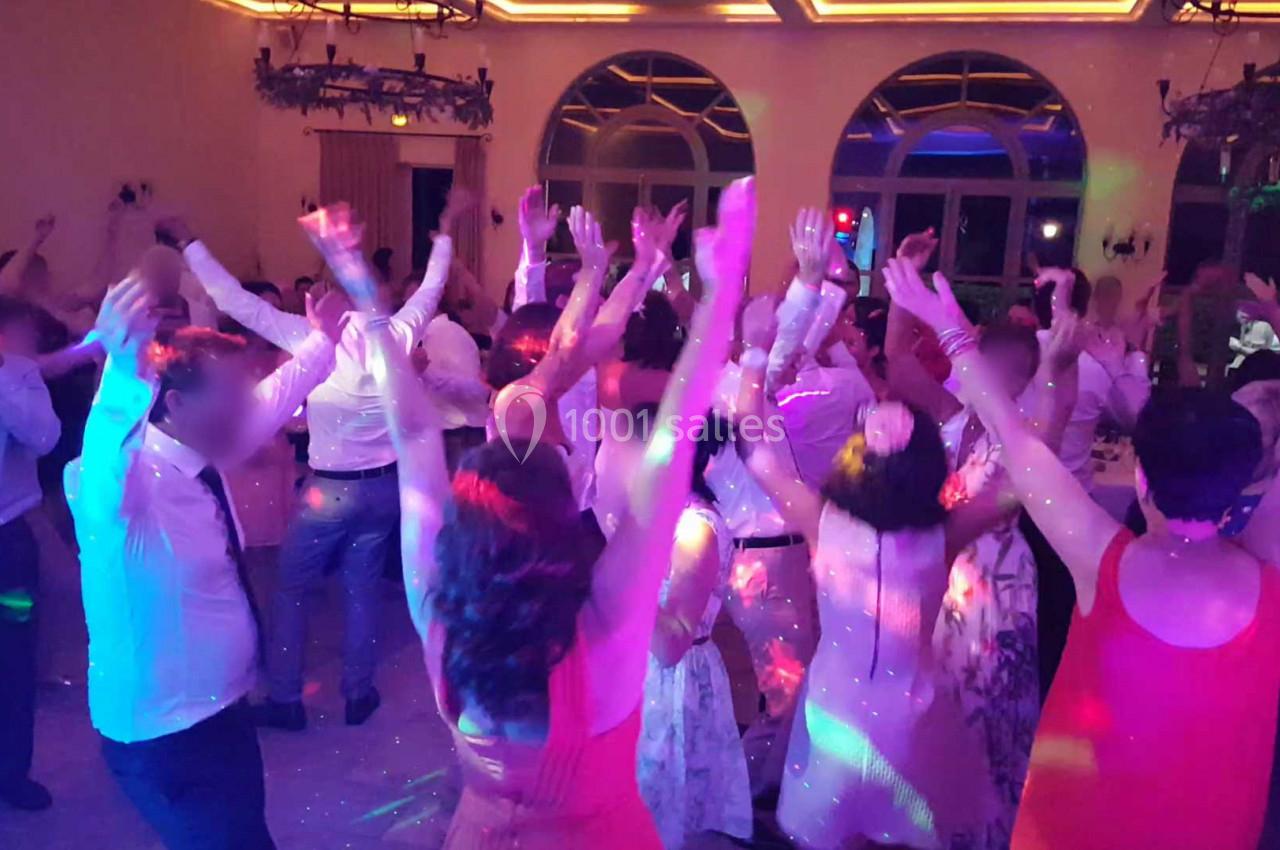 Groupe de personnes dansant sous des lumières colorées dans une salle avec de grandes fenêtres et un plafond éclairé.