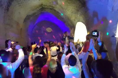 Un homme en costume est porté par une foule festive sous des guirlandes lumineuses, en extérieur de nuit.