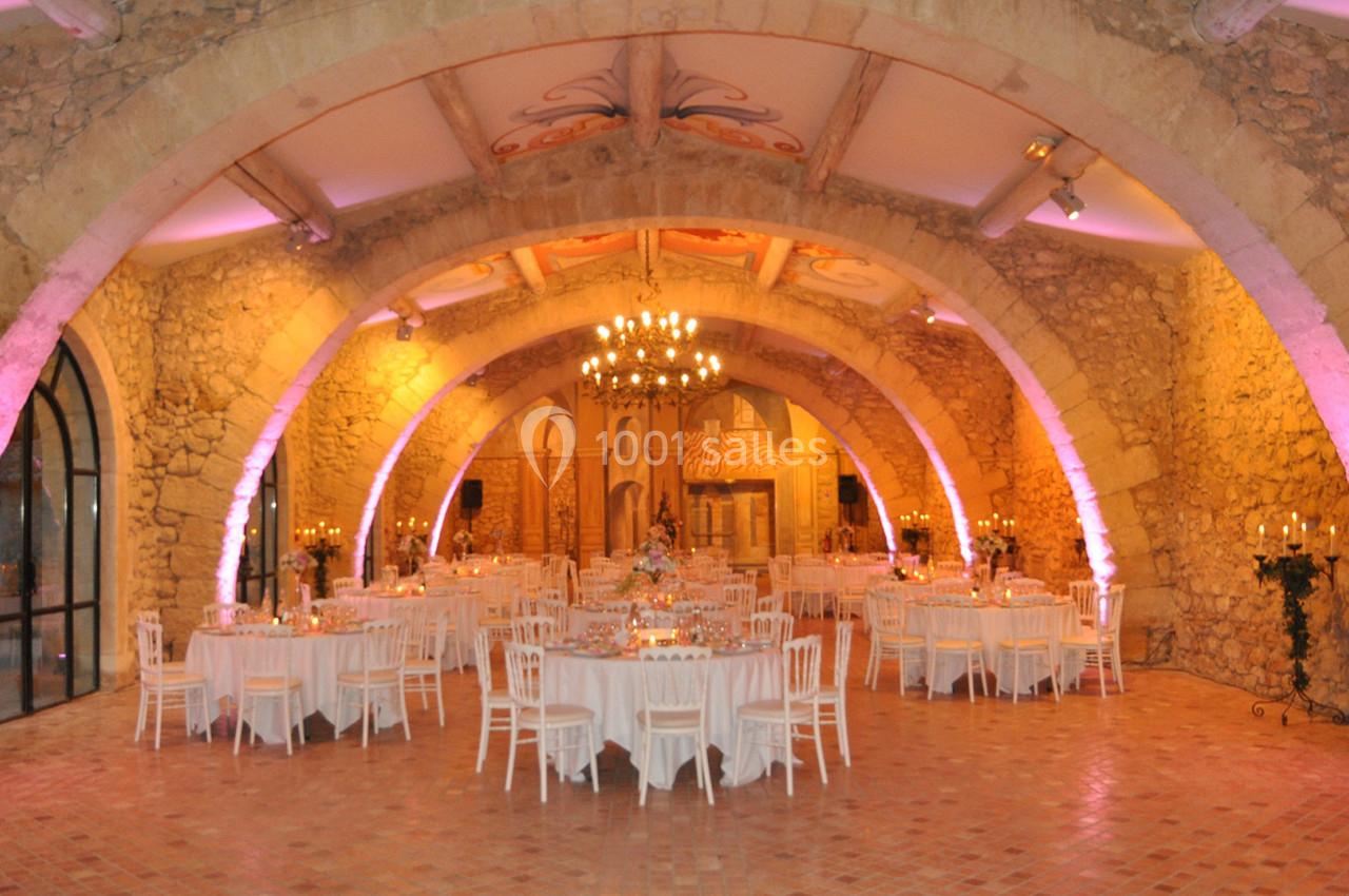 Salle voûtée en pierre avec tables rondes dressées pour un événement, éclairage chaleureux et lustre central.