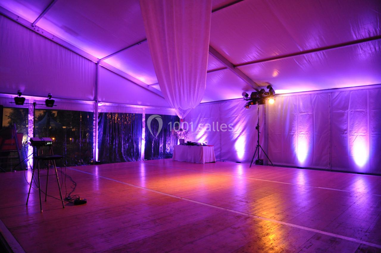 Intérieur d'une tente événementielle éclairée par des lumières violettes, avec une piste de danse en bois.