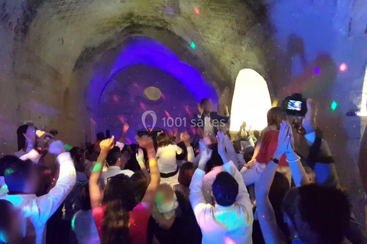 Groupe de personnes dans une salle voûtée, dansant sous des lumières colorées lors d'une fête.