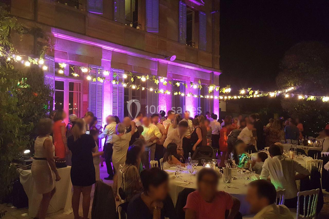 Groupe de personnes dansant et discutant lors d'une soirée en extérieur, éclairée par des guirlandes lumineuses.