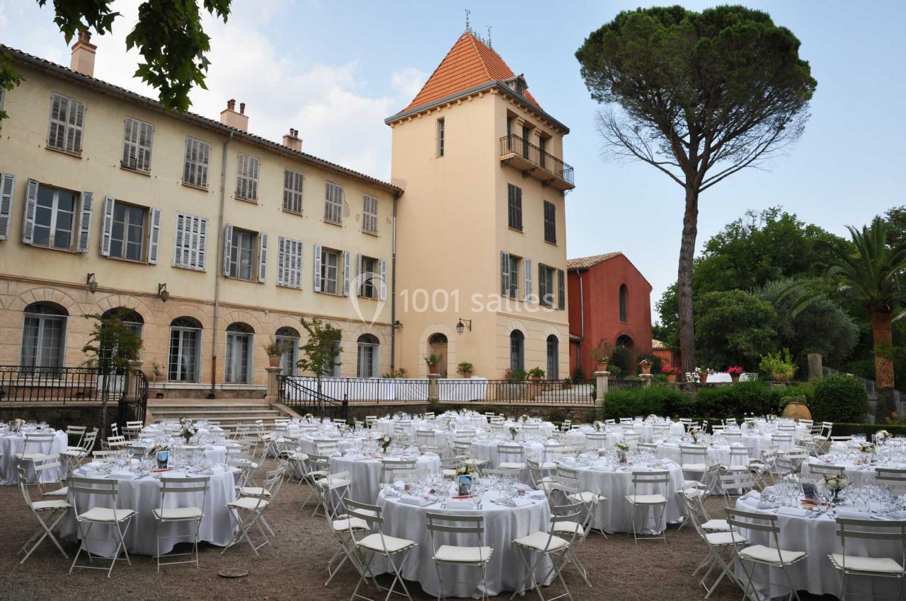 Tables rondes dressées pour un événement en plein air devant un bâtiment historique avec un grand arbre à proximité.