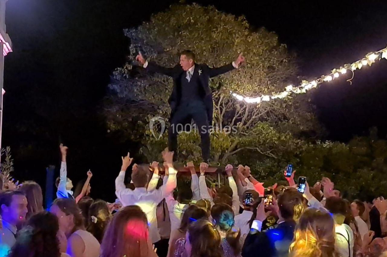 Un homme en costume est porté par une foule festive sous des guirlandes lumineuses, en extérieur, de nuit.