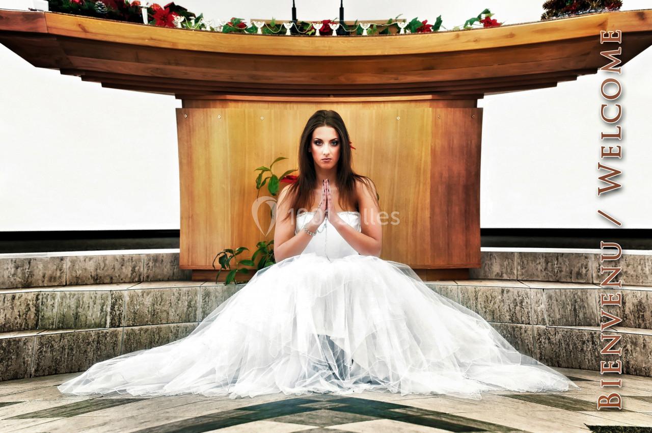 Une femme en robe blanche assise devant un autel, les mains jointes dans une posture de prière.