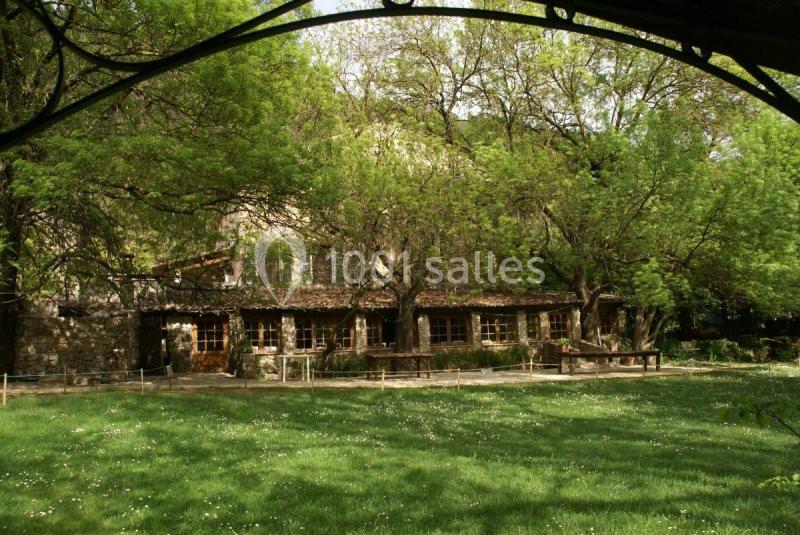 Bâtiment en pierre entouré d'arbres et d'une pelouse verdoyante sous un ciel dégagé.