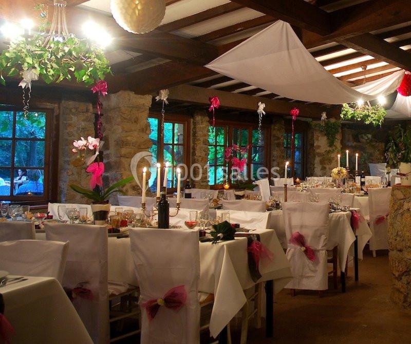 Salle de réception décorée avec des nappes blanches, des rubans roses et des chandeliers, dans un cadre rustique.