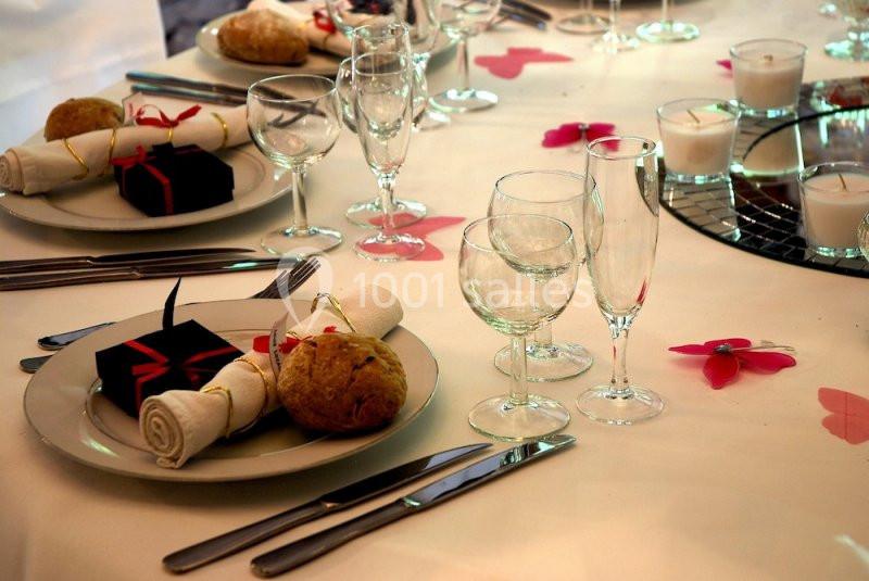 Table dressée avec des assiettes, couverts, verres, serviettes, petits cadeaux et décorations florales roses.