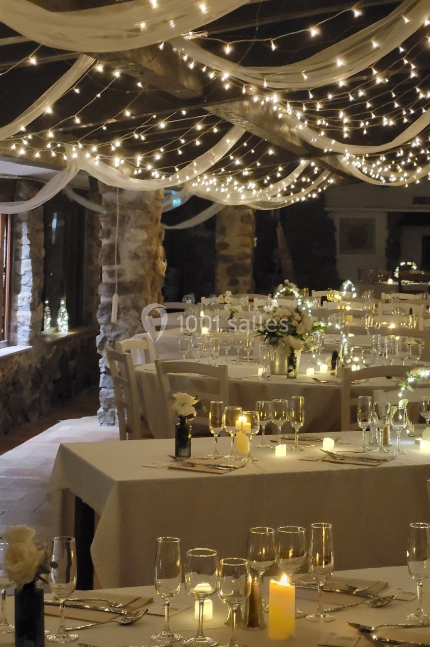 Salle de réception décorée avec des guirlandes lumineuses, des tables dressées et des centres de table fleuris.