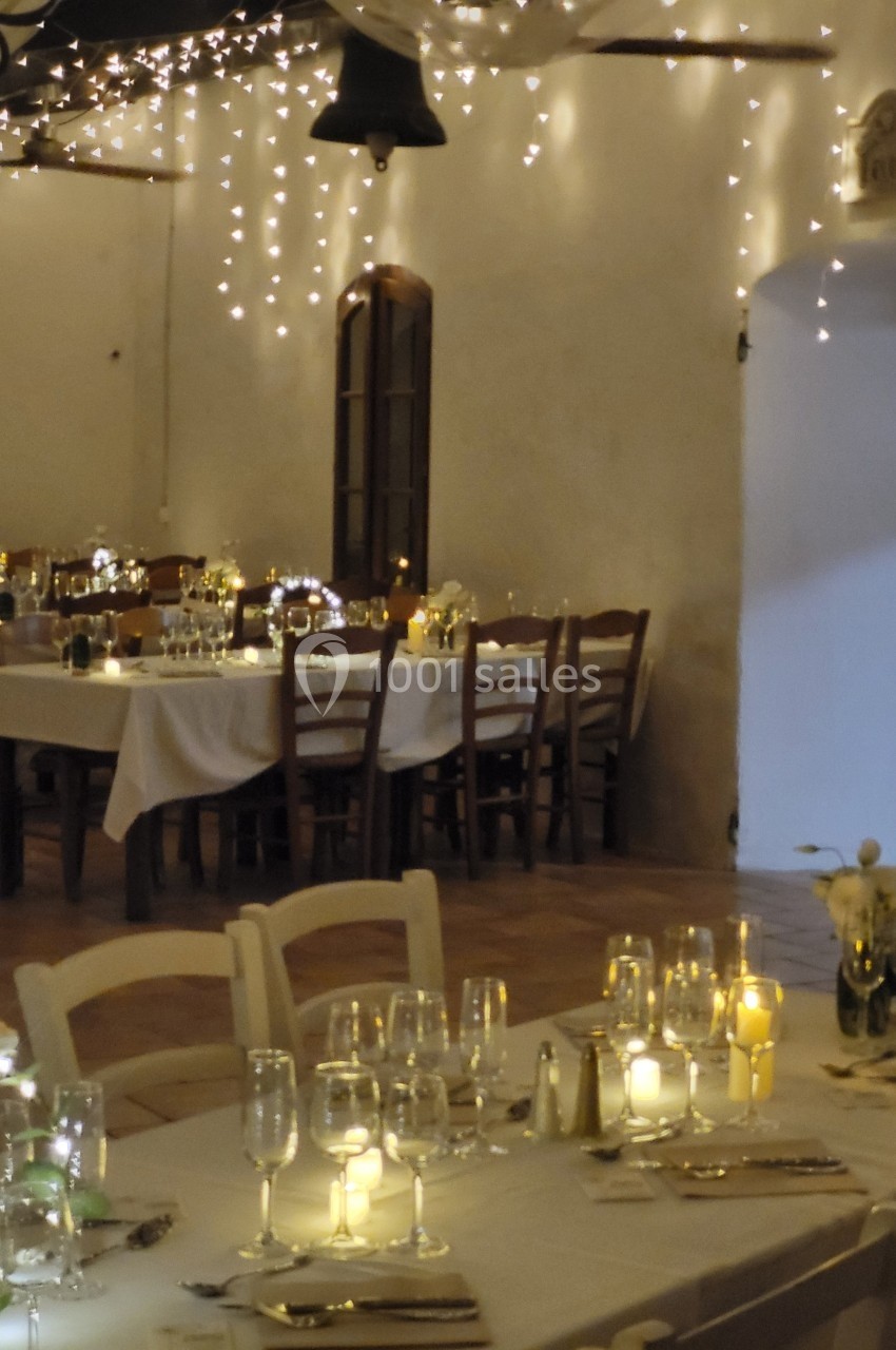 Salle de réception décorée avec des guirlandes lumineuses, des tables dressées et une ambiance chaleureuse.
