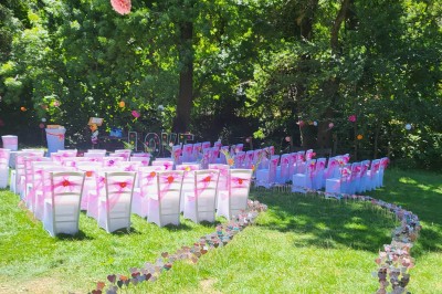 Un poney brun avec une longue crinière se tient sur une pelouse verte près d'arbres et d'un ruisseau.
