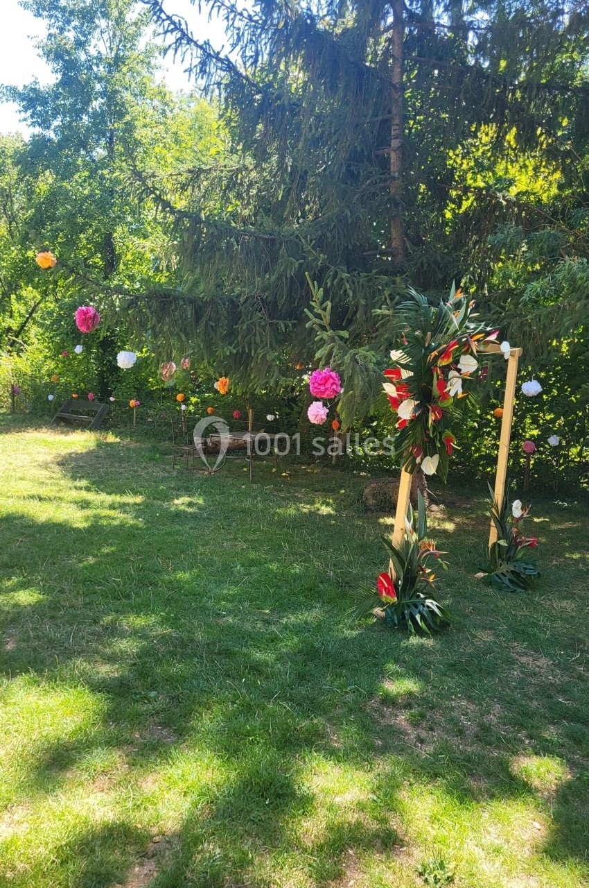 Décoration florale colorée suspendue dans un jardin verdoyant avec un cadre en bois orné de fleurs tropicales.