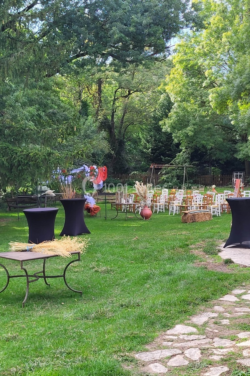 Chaises disposées en extérieur sur une pelouse entourée d'arbres, avec tables hautes décorées et bottes de paille.