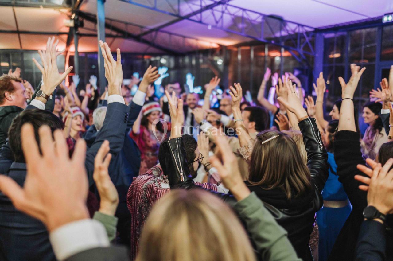 Groupe de personnes levant les bras lors d'une fête dans un espace couvert et éclairé.