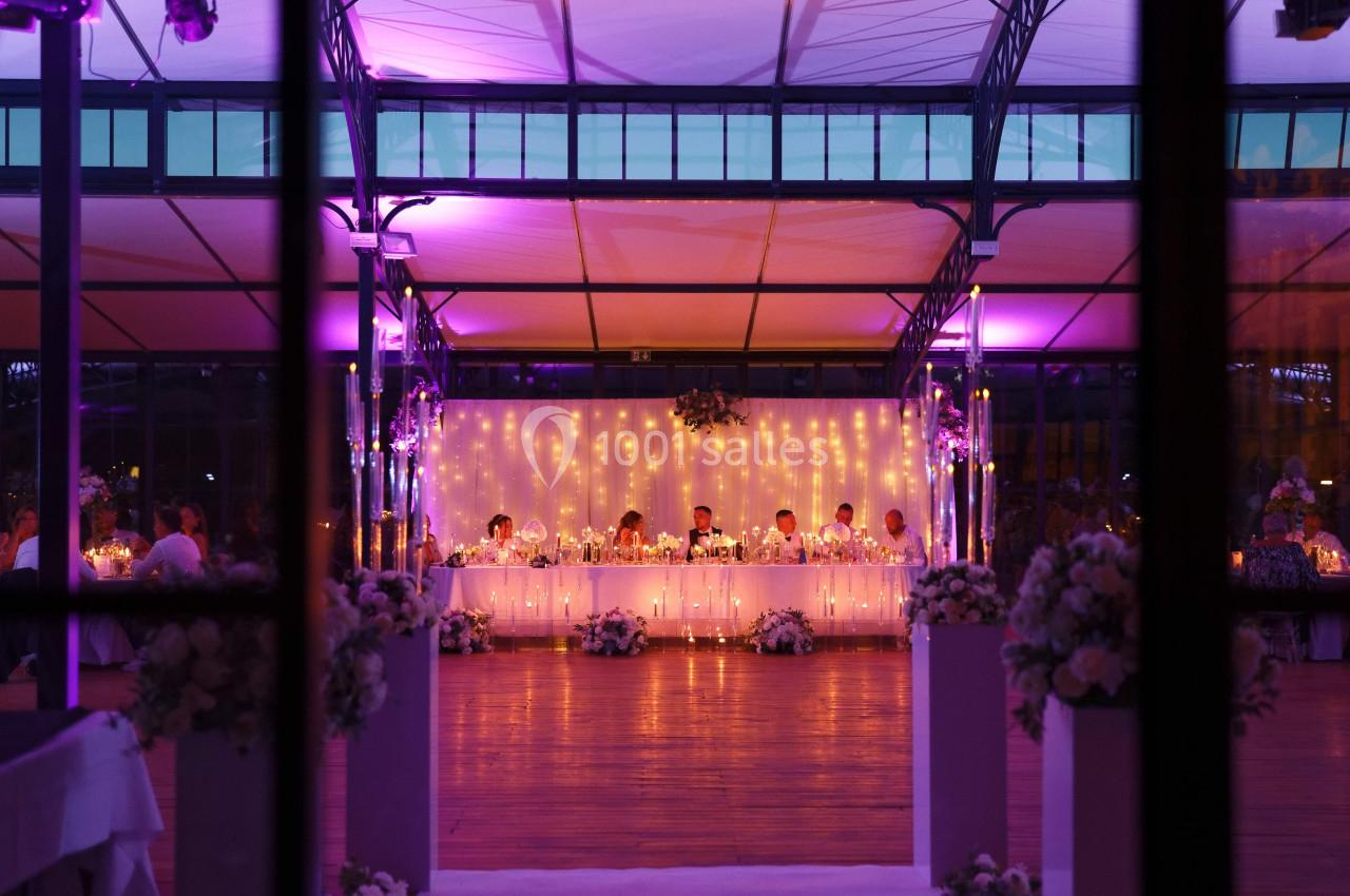 Salle de réception décorée avec des lumières tamisées et une longue table festive entourée de fleurs.