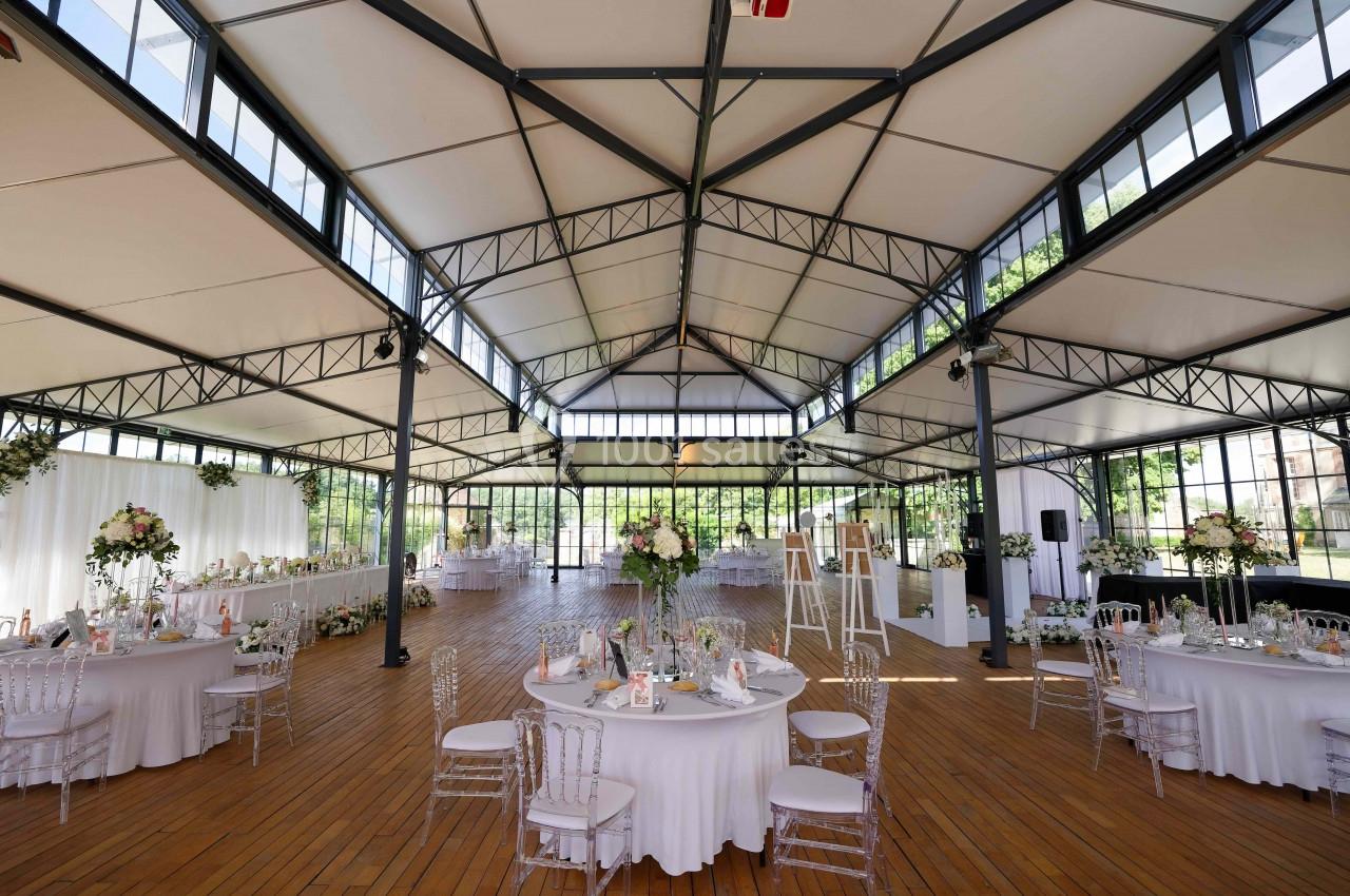 Salle de réception spacieuse avec tables rondes décorées, grandes baies vitrées et structure métallique apparente.