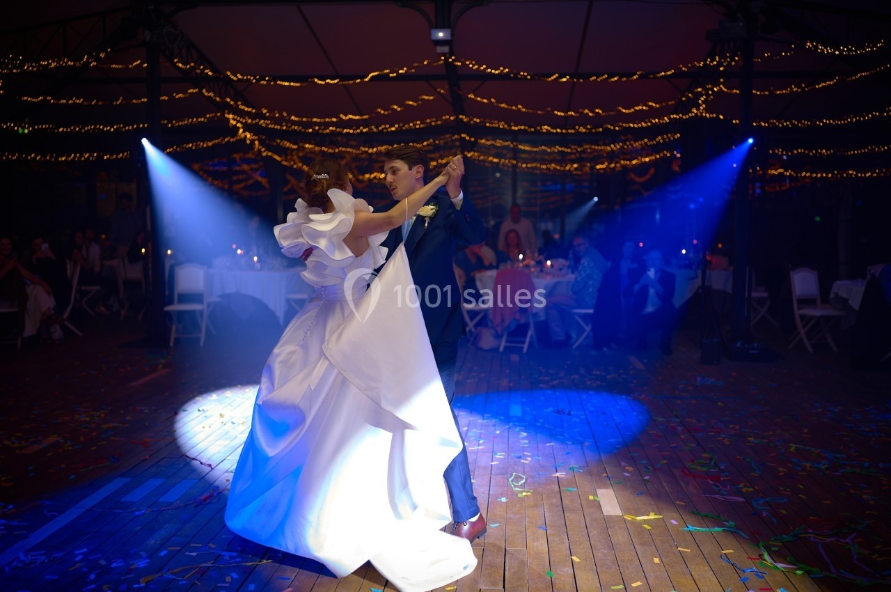 Un couple danse sous des lumières colorées dans une salle décorée de guirlandes lumineuses et de confettis au sol.
