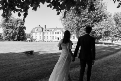 Façade d'un château en pierre et briques entouré d'une pelouse et d'arbres sous un ciel bleu clair.