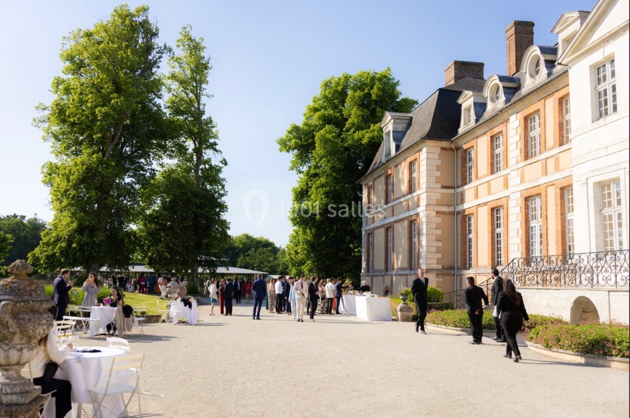 Groupe de personnes rassemblées devant un château en pierre, entouré de verdure, par une journée ensoleillée.
