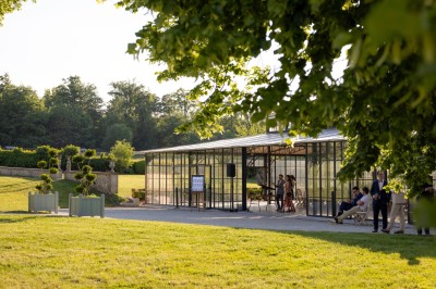 Façade d'un château en pierre et briques entouré d'une pelouse et d'arbres sous un ciel bleu clair.