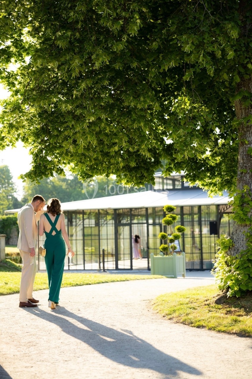 Un couple marche sur un chemin ensoleillé près d'une serre entourée de verdure.