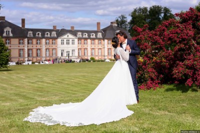 Façade d'un château en pierre et briques entouré d'une pelouse et d'arbres sous un ciel bleu clair.