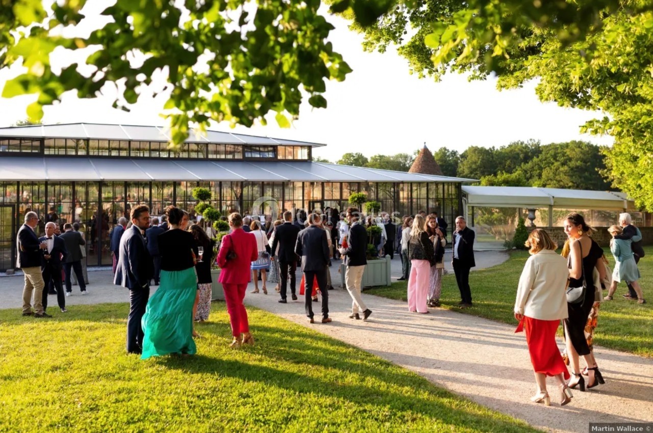 Groupe de personnes rassemblées devant une grande serre vitrée, entourée de verdure, par une journée ensoleillée.
