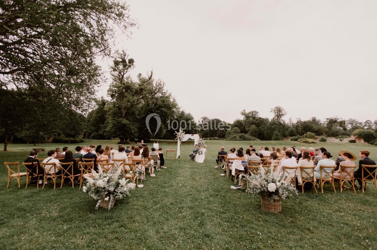 Cérémonie de mariage en plein air avec invités assis sur des chaises en bois, entourés de verdure et de décorations florales.