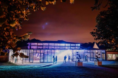 Façade d'un château en pierre et briques entouré d'une pelouse et d'arbres sous un ciel bleu clair.