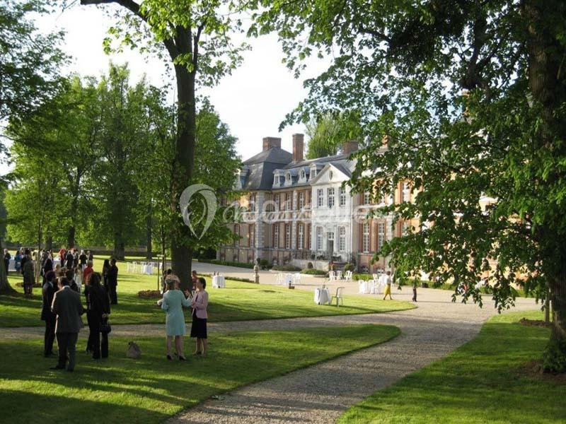 Des personnes discutent dans un jardin verdoyant devant un grand bâtiment de style classique par une journée ensoleillée.