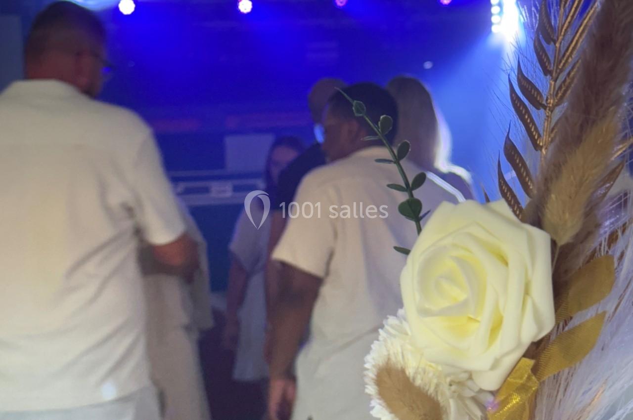 Des personnes en tenue blanche dansent sous des lumières colorées, avec un bouquet de fleurs séchées au premier plan.