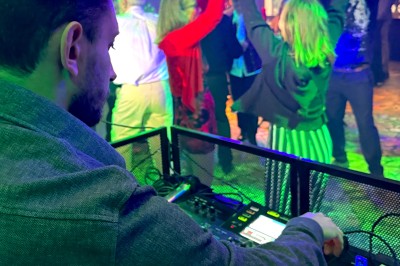 Main ajustant les réglages sur une table de mixage DJ illuminée par des lumières colorées.